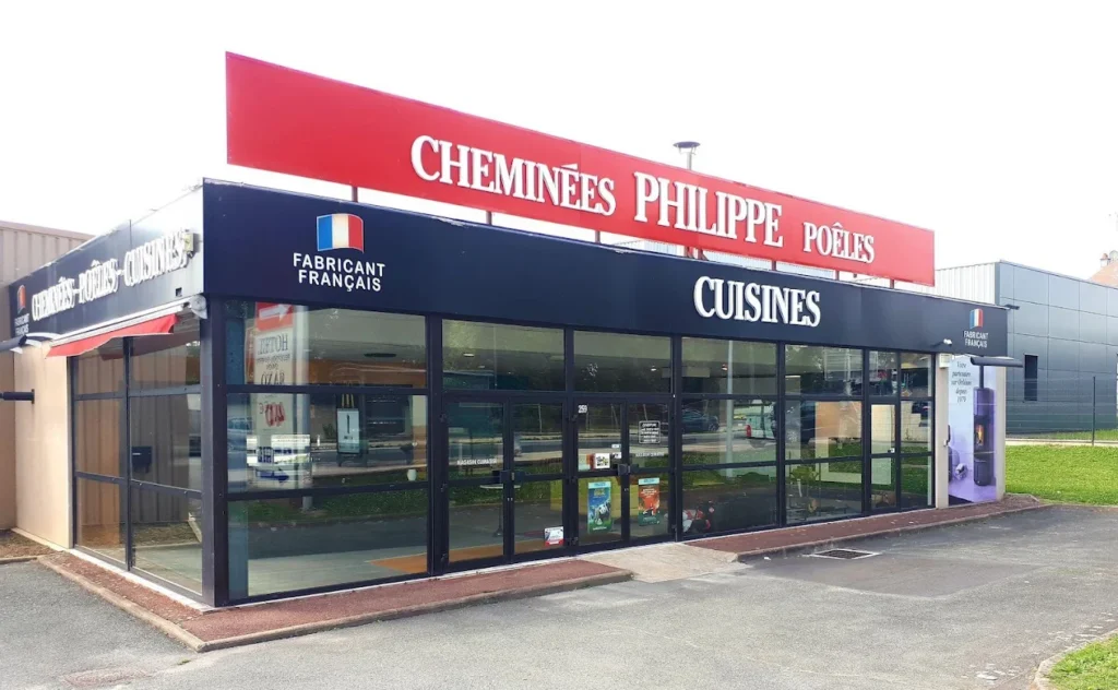 Magasin spécialisé en cheminées et cuisines, façade avec enseignes CHEMINÉES PHILIPPE et CUISINES, grande baie vitrée et entrée en verre. tubage cheminée? cannot. Include keyword naturally: "tubage cheminée" integrated. But image shows storefront; we can mention site related. Alt text: "Magasin CHEMINÉES PHILIPPE avec CUISINES, facade vitrée, inscription Fabricant Français; tubage cheminée en contexte informatif." Ensure natural. Max 125 chars. Let's craft: "Magasin CHEMINÉES PHILIPPE et CUISINES, façade vitrée et enseignes rouges et bleues, facade commerciale." Need include keyword seamlessly: "tubage cheminée" as part of description though not visible. We must describe truthfully. It's tricky to include keyword if not visible. The rule says integrate keyword when provided; build around. Could say: "Façade d’un magasin CHEMINÉES PHILIPPE et CUISINES; guide sur tubage cheminée en ligne." but image itself doesn't show guide. But we can say "enseigne" and mention tubage cheminée as topic related. It's acceptable? Should not invent content. I will include phrase: "Façade de magasin CHEMINÉES PHILIPPE et CUISINES" and add "tubage cheminée (thème du guide)". Let's craft: "Façade de magasin CHEMINÉES PHILIPPE et CUISINES, vitrines et enseignes, sujet tubage cheminée traité dans le guide." Keep length. ~112 chars. French. Let's output.